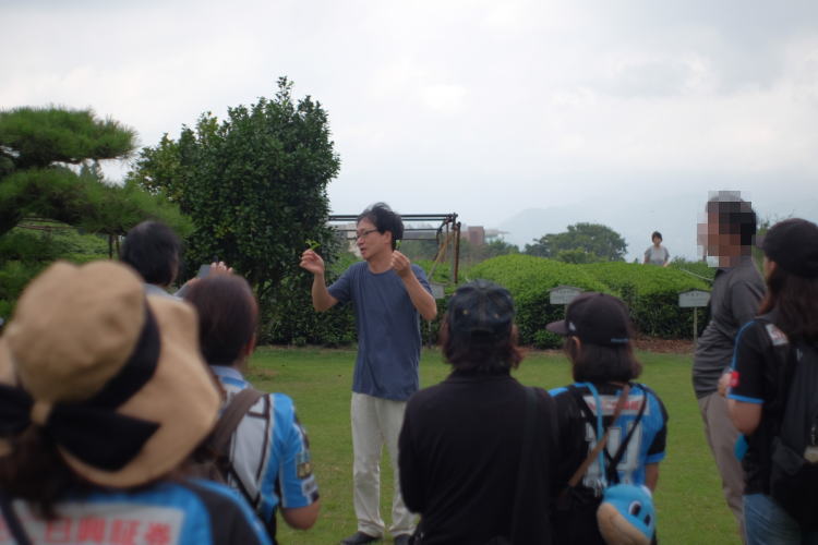 The manager of the tea facility explaining to the guests how to pick green tea leaves